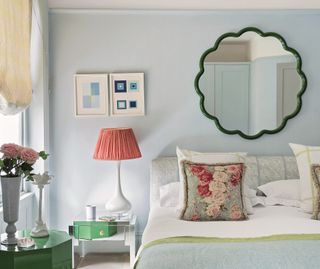 A bedroom with light blue walls, a wavy mirror, and a lamp with a red shade