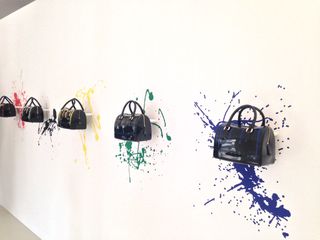 A collection of black handbags displayed on a white wall with a splash of colour behind each of it