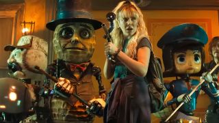 a woman with long blonde hair holds a gun surrounded by strange puppet oddballs