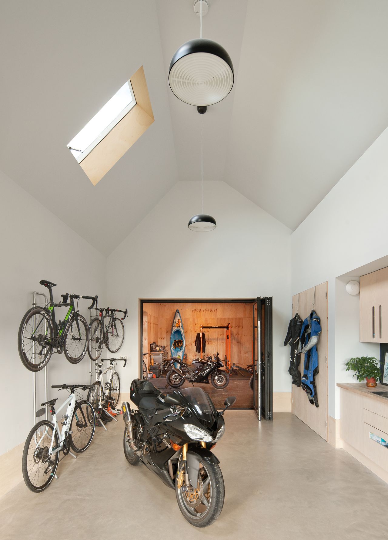 A workshop with tall white walls and a vaulted ceiling, featuring a motorbike and push bikes on the wall