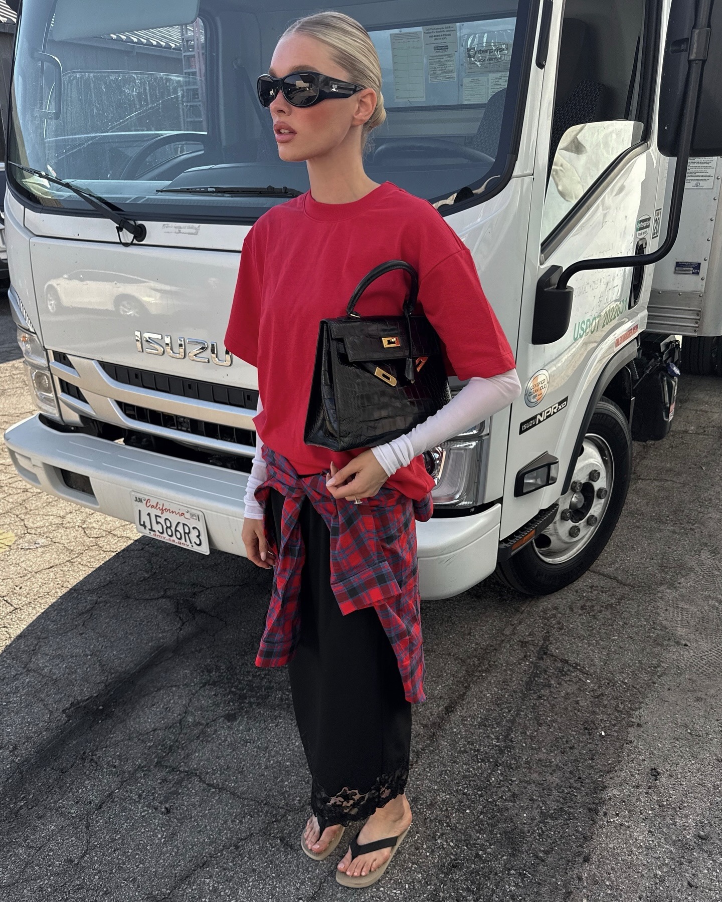 Elsa Hosk wearing a red T-shirt, plaid shirt around the waist, and long lace-trim skirt with flip-flops