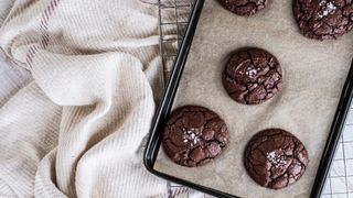 A baking tray of freshly baked chocolate cookies, on a wire cooling rack