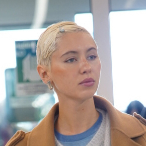 Iris Law wearing a tan coat, gray cardigan, beige jeans, blue sneakers, and a lime Louis Vuitton speedy bag 