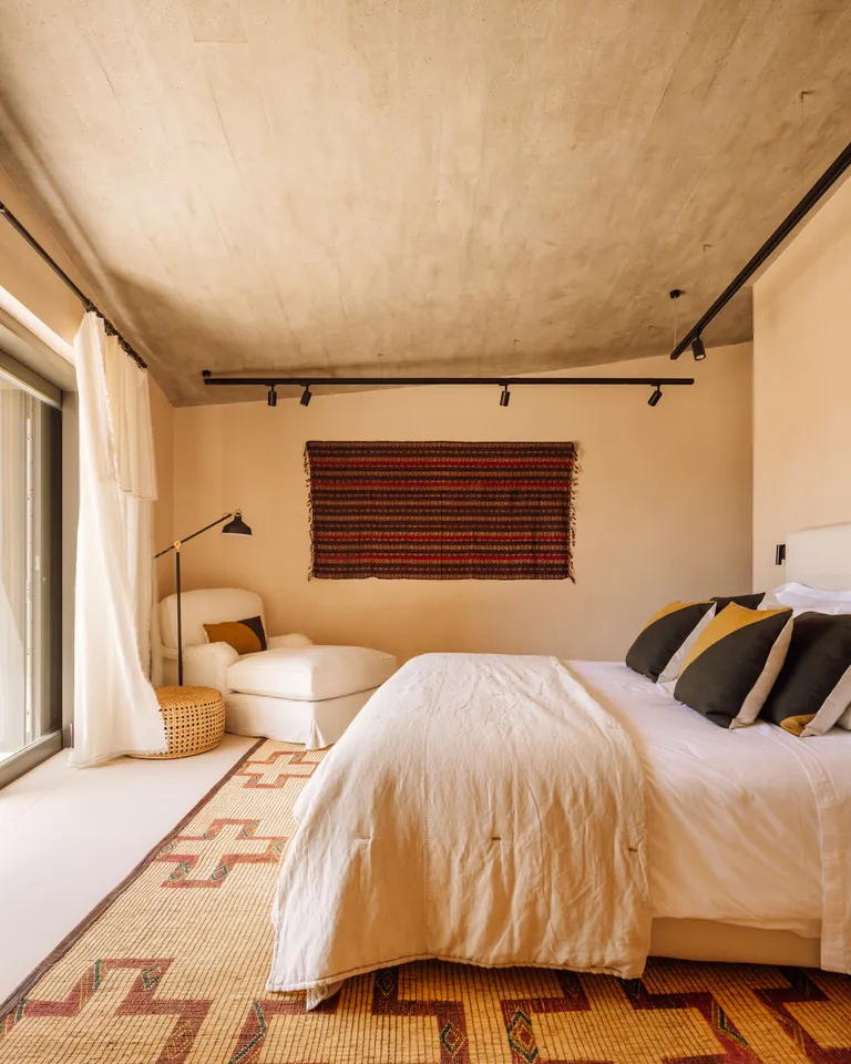 A neutral bedroom with rustic patterned rug and wall hanging