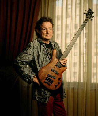 Jack Bruce pictured holding a bass guitar in a hotel room