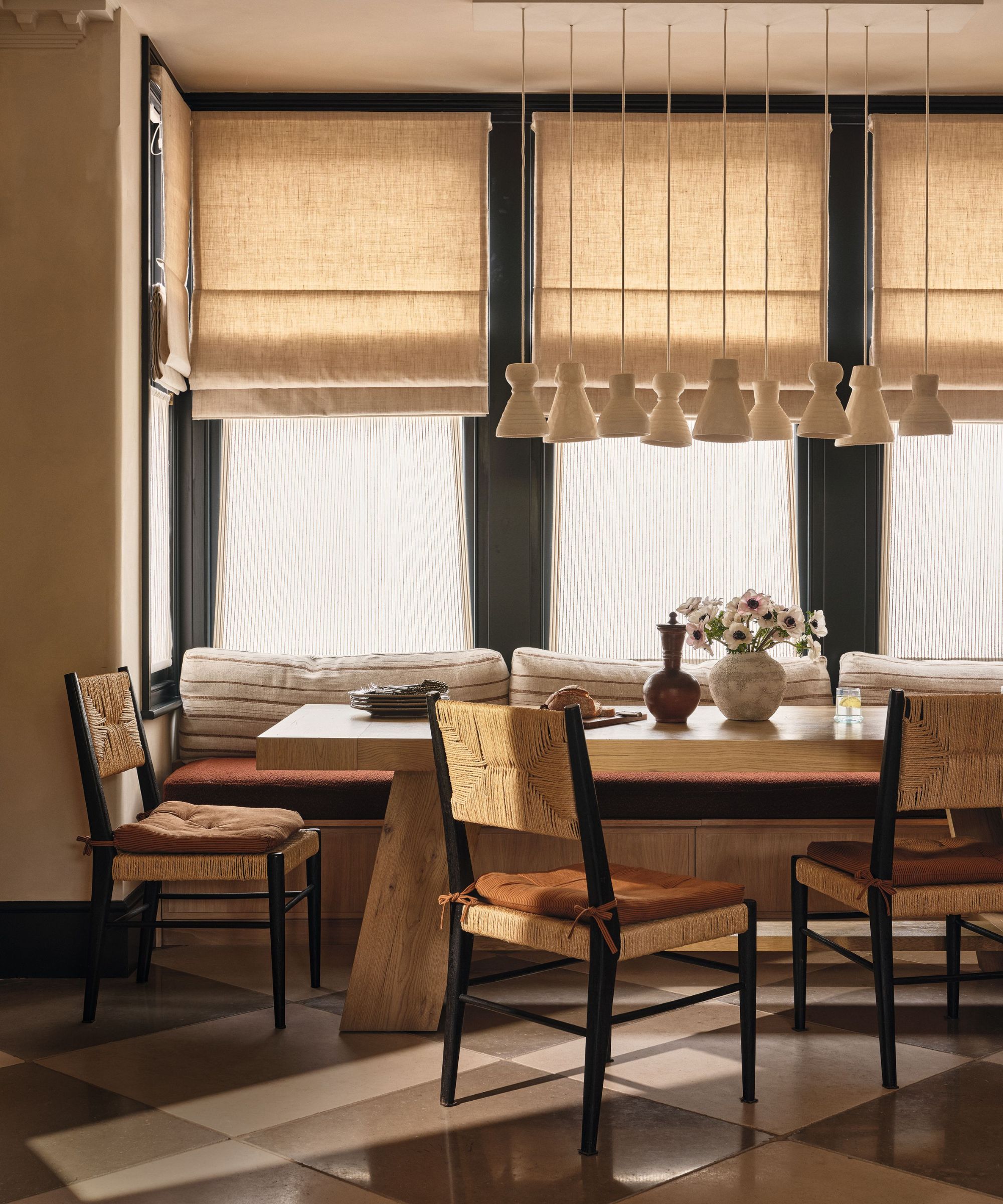 a calm earthy dining area with bespoke dining bench beneath a large window on checkerboard stone floor