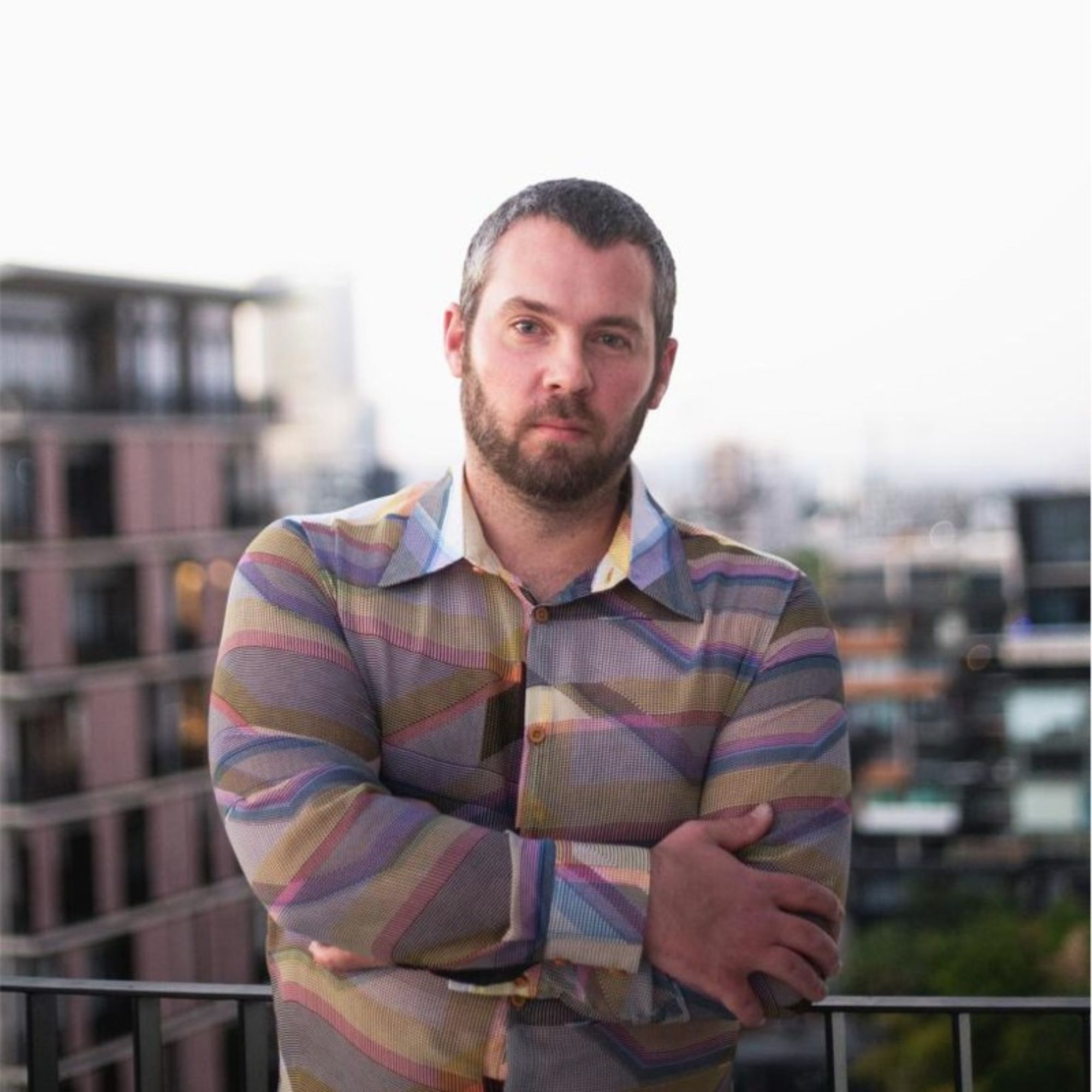 A picture of Chris Kinlaw in a checked shirt, with gray buildings in the background