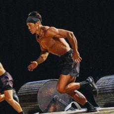 a shirtless man (amotti) running, while large cylinder weights rest behind him, in 'physical 100' season 2