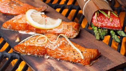 Three pieces of grilled salmon on a cedar plank with lemon slices and zest 