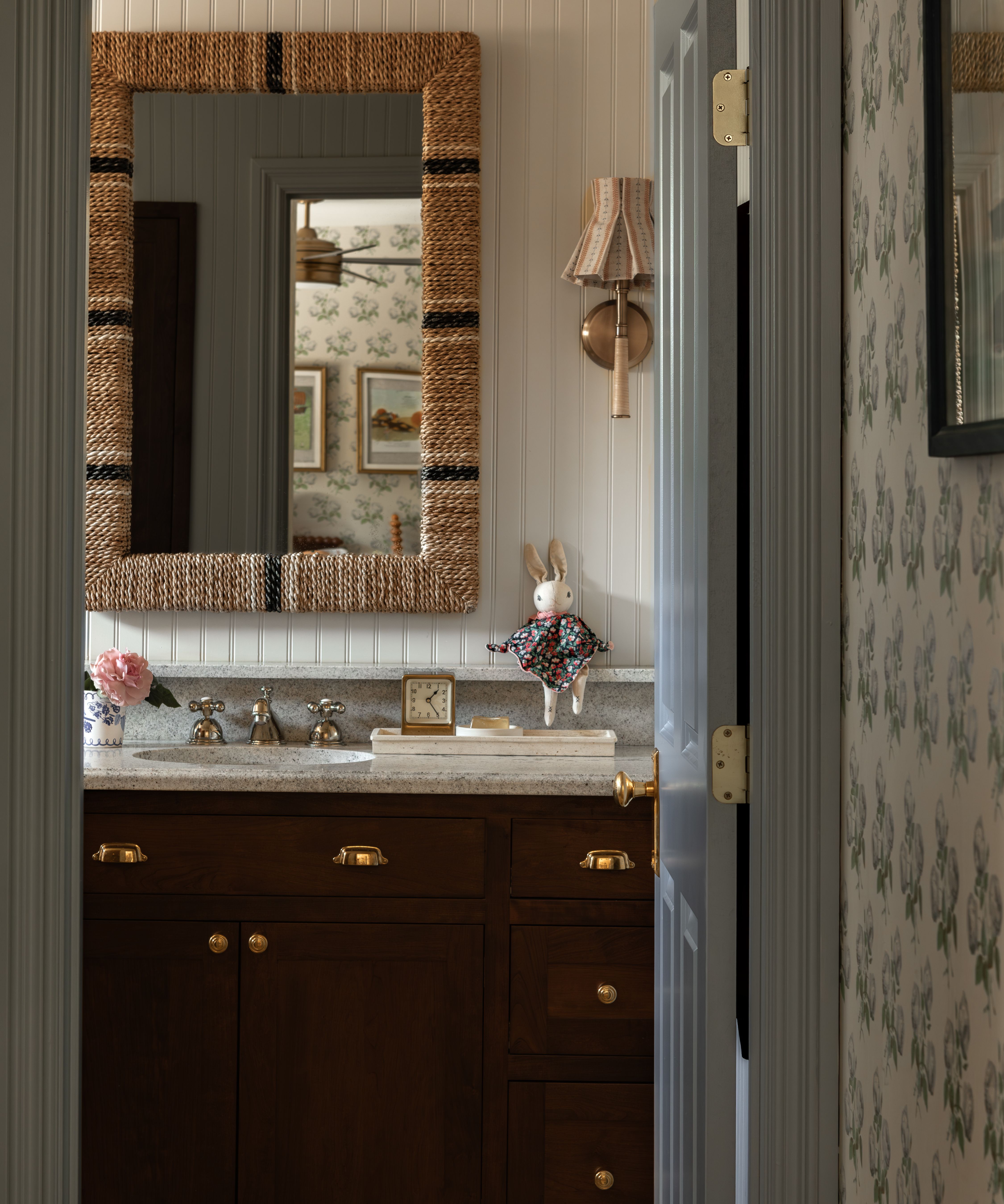 a floral bedroom leading onto a paneled bathroom with a dark wooden vanity