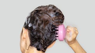 A woman pictured shampooing her hair and using a scalp massaging brush