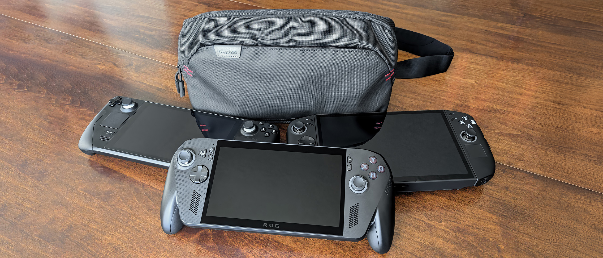 Tomtoc Arccos G-47 Travel Bag behind the Steam Deck, Legion Go 2, and Xbox Ally X.