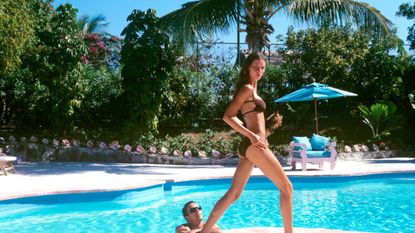 woman wearing a swimsuit walks beside a swimming pool during summer