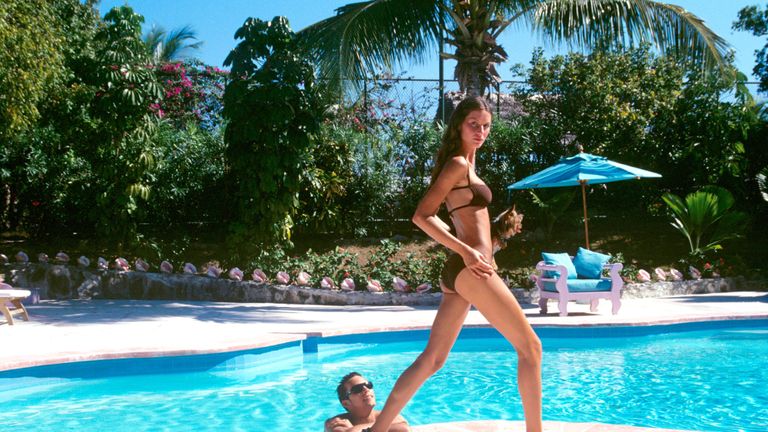 woman wearing a swimsuit walks beside a swimming pool during summer