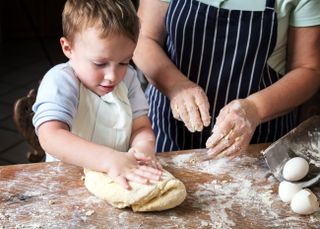A young blonde boy kneading dough with an adult.