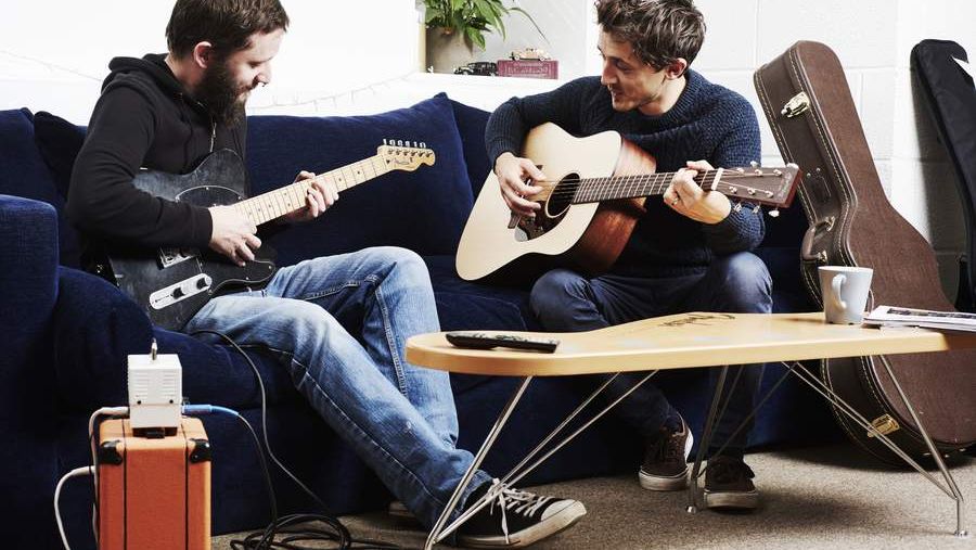 Two guitarists jamming on a sofa