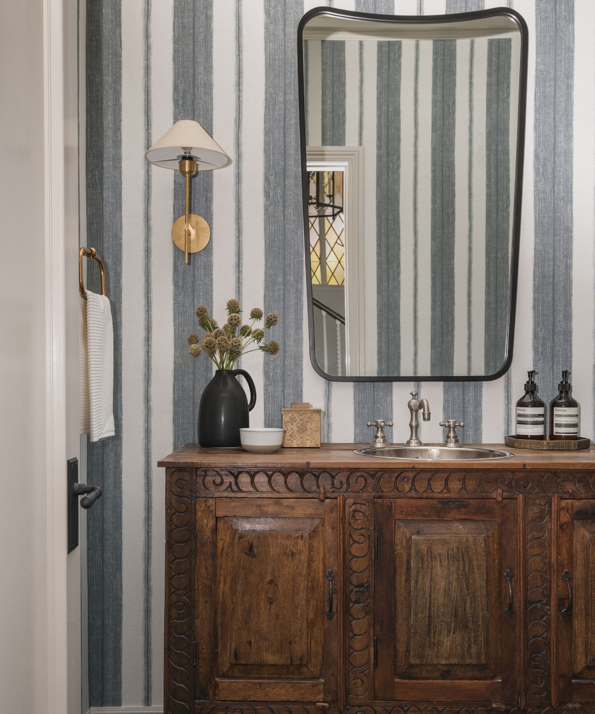A powder room with dark blue and white striped wallpaper, a large vanity mirror and a vintage wooden dresser