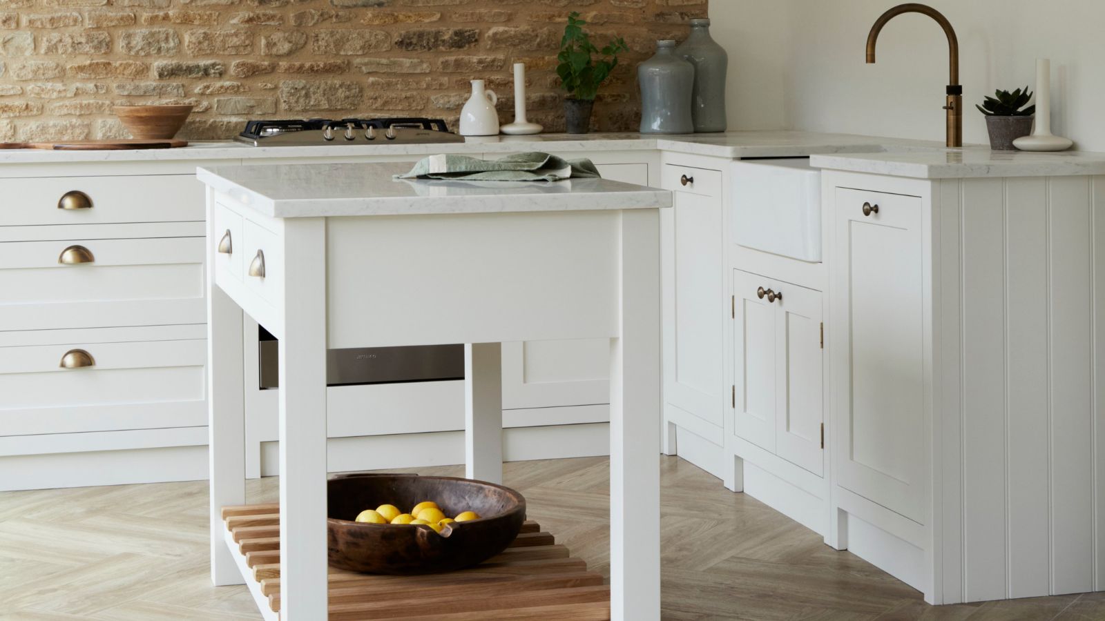 Small white portable kitchen island with marble top and slatted shelf, set in a bright shaker kitchen with brass handles and stone flooring.