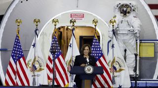 kamala harris surrounded by american flags at a podium, spacesuit to the side