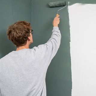 man painting blue grey wall with roller