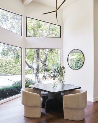 Dining area with black-framed architectural windows, round mirror, and delicate pendant light