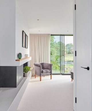 view into a bedroom with full height glazed windows and a grey armchair in front of the window