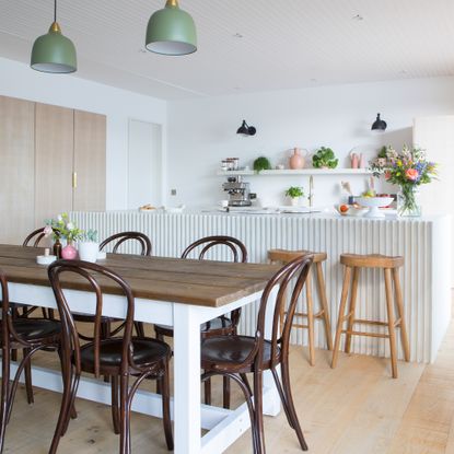 A modern kitchen diner with microcement island, wooden bar stools, dark wooden dining table and chairs and sage green pendant light fixtures