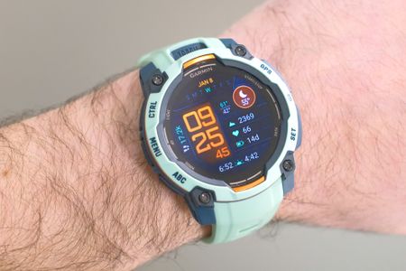 Close-up of the Garmin Instinct 3 smartwatch in orange and teal on a user's wrist with the default screen shown