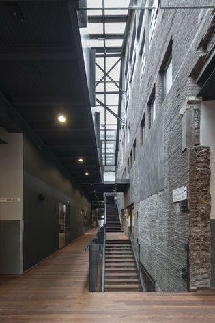 View from the inside of the Cultural Centre, Dordrecht, wooden floor, black stairwell, rustic stone walls, spotlights, glazed roof with black metal framework