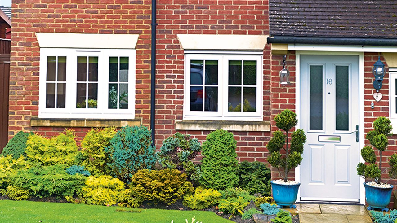 Front exterior of a red brick house with a border of shrubs in the front garden