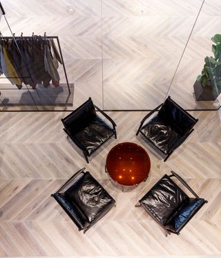 View from above of a round amber coloured table and black chairs at Dunhill's HQ. Part of the showroom with a rail of clothing and a plant can also be seen through the glass partitions