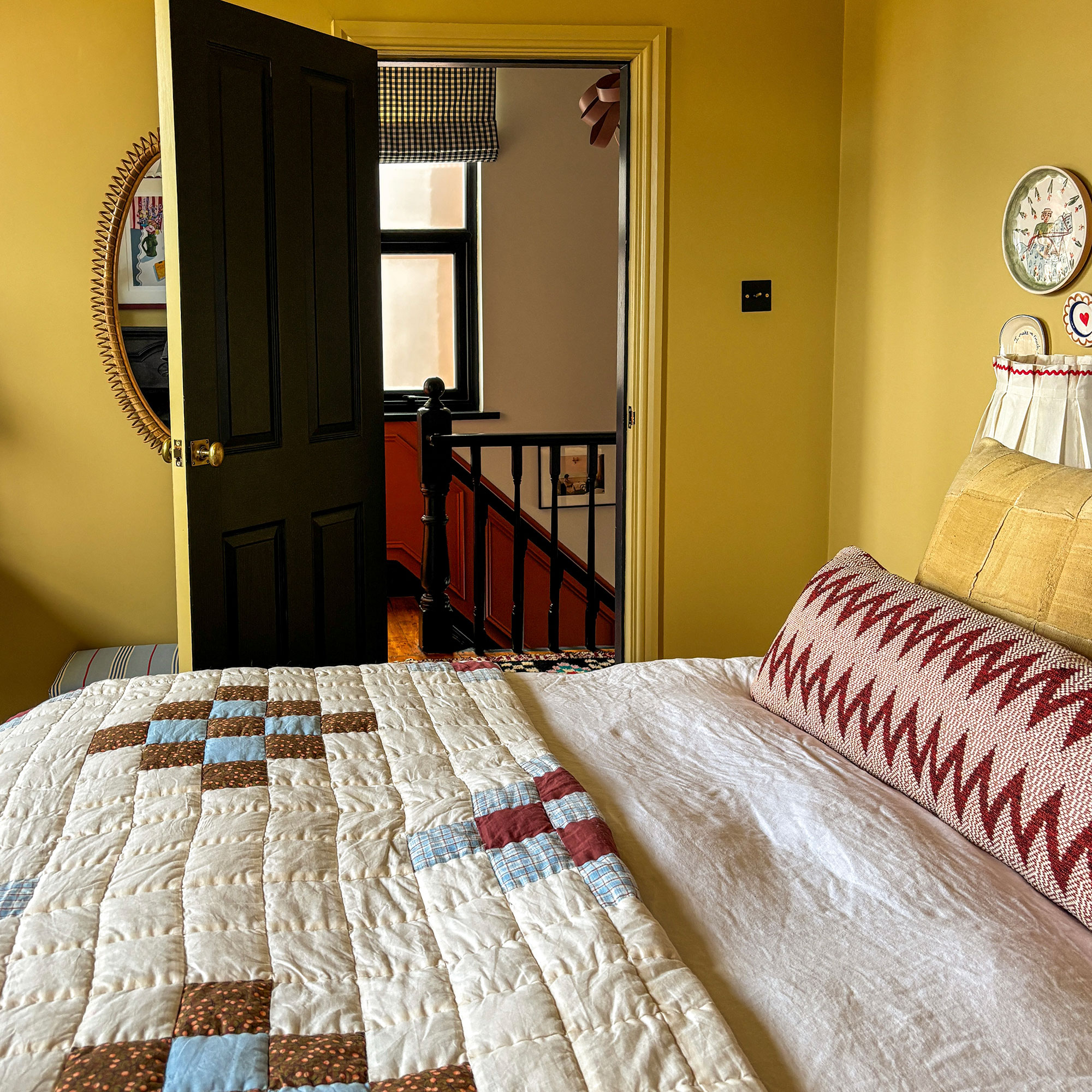 Yellow bedroom with patchwork quilt and patterned bolster cushion on bed