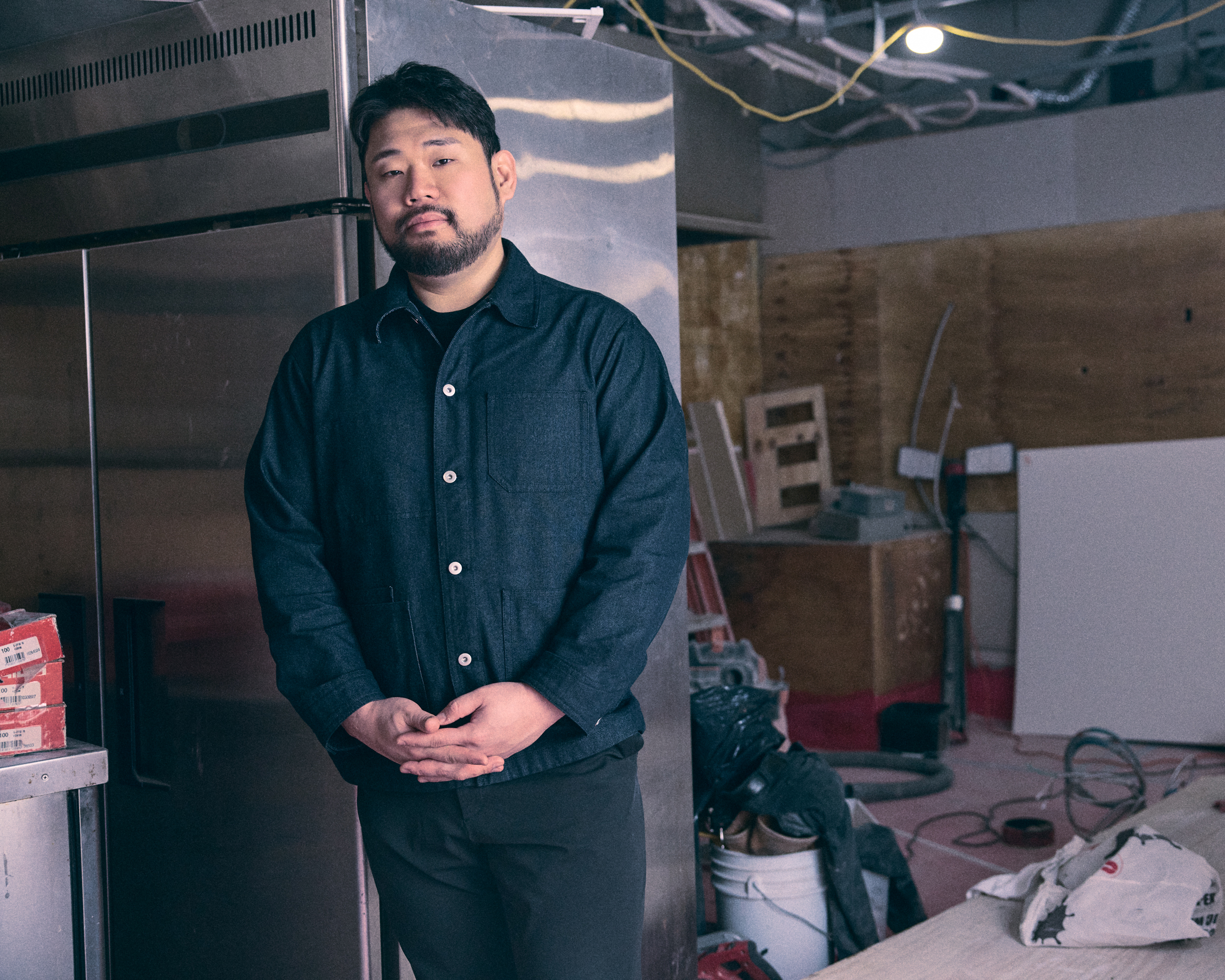 Chef Lee Ha-sung, nicknamed Culinary Monster, poses with his hands intertwined while standing in a half-built restaurant, in a promotional portrait for 'Culinary Class Wars.'
