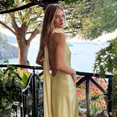Model @rosiehw stands outside on a balcony in Italy wearing a satin maxi dress in butter yellow.