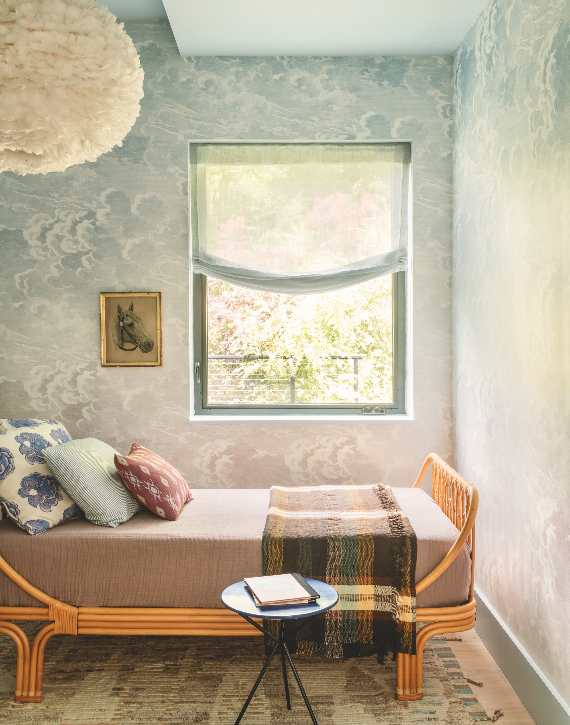 Bedroom with cloud wallpaper, in a baby blue color, with a wooden bed frame with a ruffled cream fabric lamp hanging above.