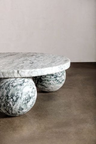 The image shows half of the table. The half shown is 2 marble spheres holding up the round table top. Photographed in a room with white wall and brown floor