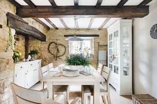 dining room with beams and exposed stone walls with table with big wild flower arrangement and white cabinet