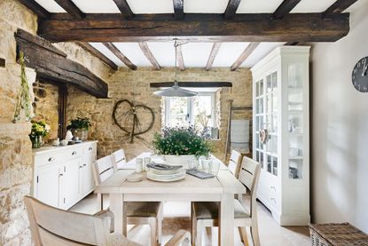 dining room with beams and exposed stone walls with table with big wild flower arrangement and white cabinet