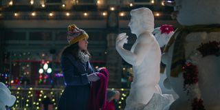 Lacey Chabert as Kathy Barrett, holding a red scarf while standing in front of a life-like snowman in 'Hot Frosty.'