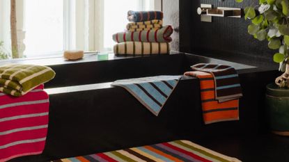 A bathroom with a black tub surrounded by colorful striped towels