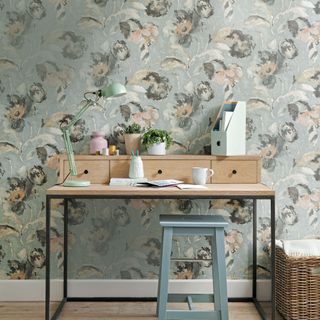 a subtle country style scheme with floral wallpaper and a wooden desk and stool and floral wallpaper