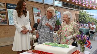 Queen Elizabeth II considers cutting a cake with a sword, lent to her by The Lord-Lieutenant of Cornwall, Edward Bolitho