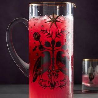 A Lauren McIntosh Glass Pitcher with a black crow design and a red drink