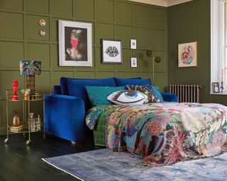A living room by Snug sofa using velvet blue sofa bed, khaki green wall panel decor and brass bar cart