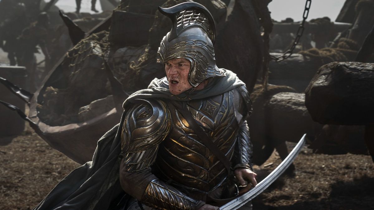 Robert Aramayo as Elrond in battle, holding a sword in his left hand and wearing a helmet in Rings of Power Season 2. 