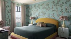 Bedroom with pale blue floral wallpaper, yellow velvet upholstered headboard and teal bedding