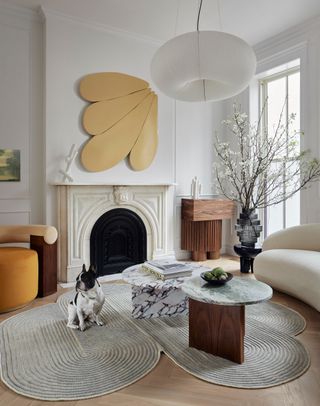 a living room with an irregularly shaped rug, yellow wall art and accent chair, and a curved white sofa