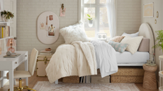 a dorm room with a white brick wall, a bed with several pillows on top and storage underneath, and a desk to the left