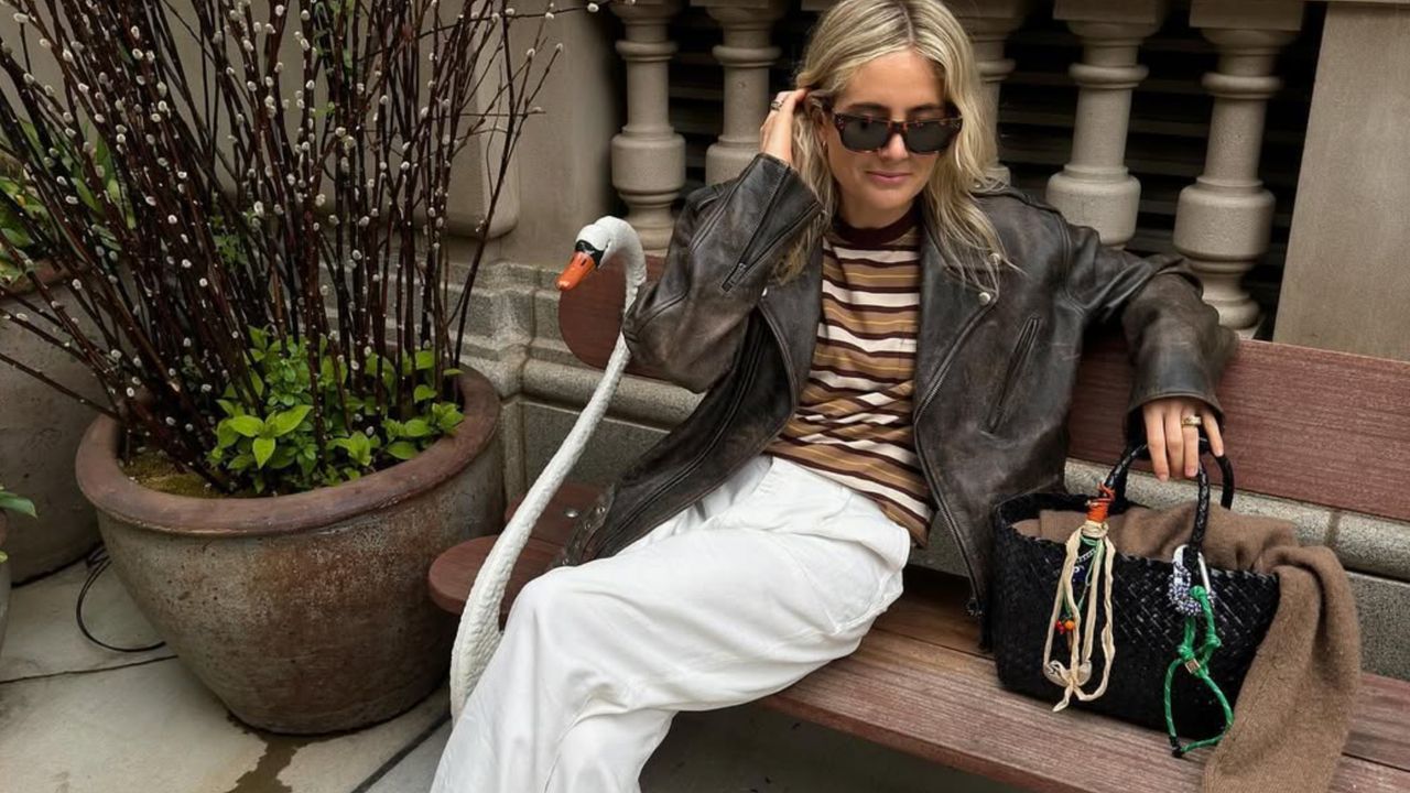 Lucy Williams wearing a brown leather jacket, a striped tee, and white jeans.