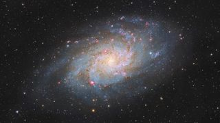 A large spiral galaxy with sweeping spiral arms and a glowing core shines against a sea of stars.